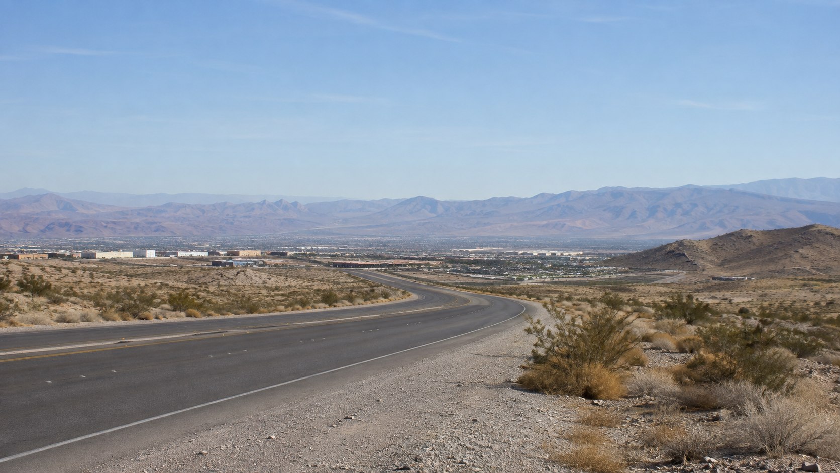 Open desert roadway descending toward a valley and surrounding mountains